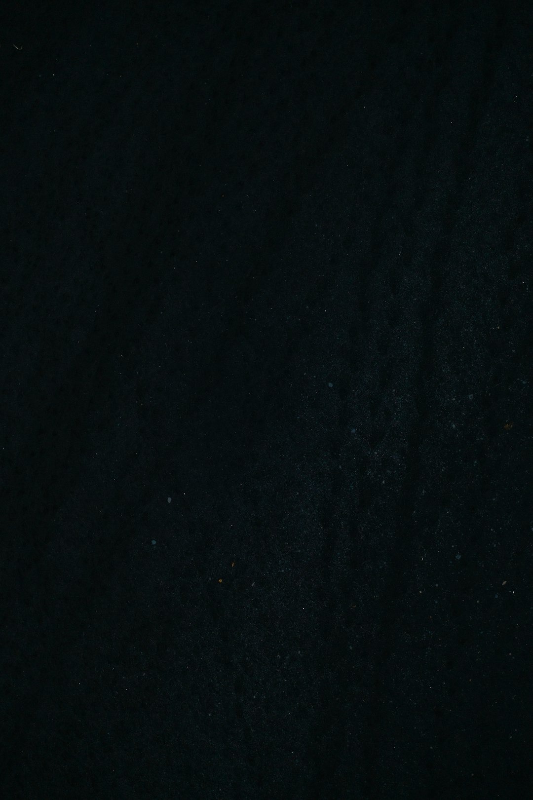 Dark textured surface with subtle green and black variations.